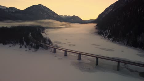 西爾文斯坦水庫 (sylvenstein reservoir bridge) 位於奧地利巴伐利亞高山區 (bavarian austrian alps) 在冬天有雪,山脈和晴朗的藍色水域,在日落時