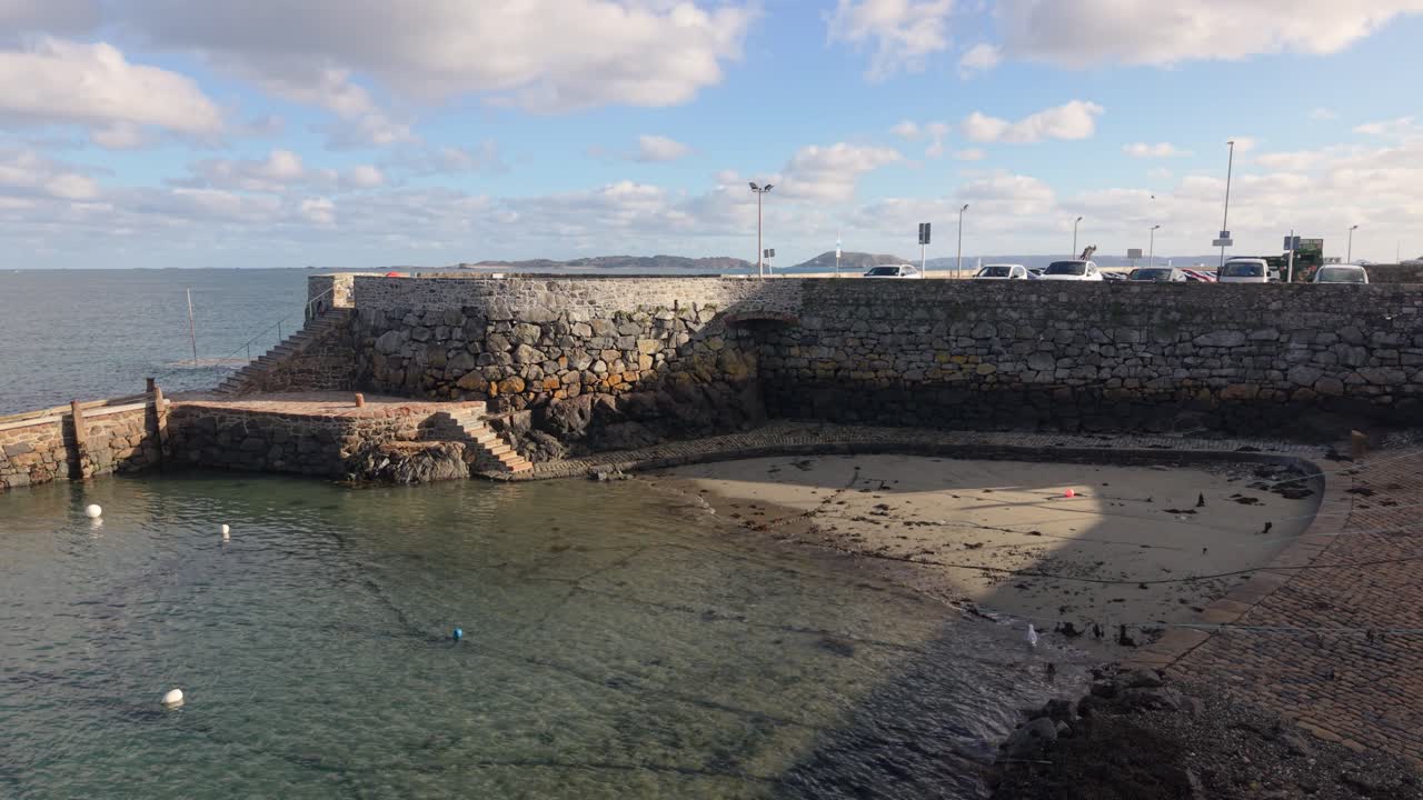 Salerie Corner St Peter Port Guernsey tiết lộ cảnh quay drone về bến cảng cổ xưa vào lúc thủy triều giữa, dưới nắng vàng với mặt nước trong xanh lặng sóng và tầm nhìn ra đảo Herm