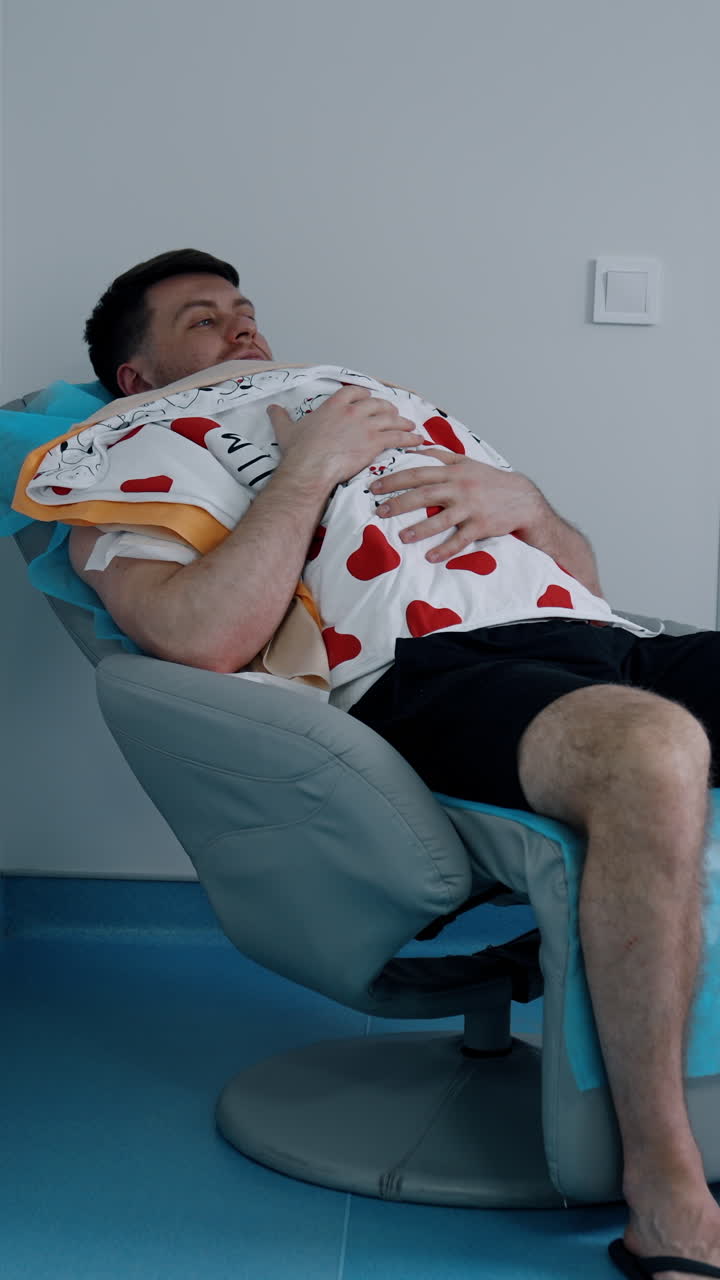 Caucasian man sits in a chair holding a newborn child on the chest. Loving dad taking care of his baby. Vertical video