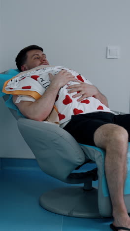caucasian man sits in a chair holding a newborn child on the chest. loving dad taking care of his baby. vertical video