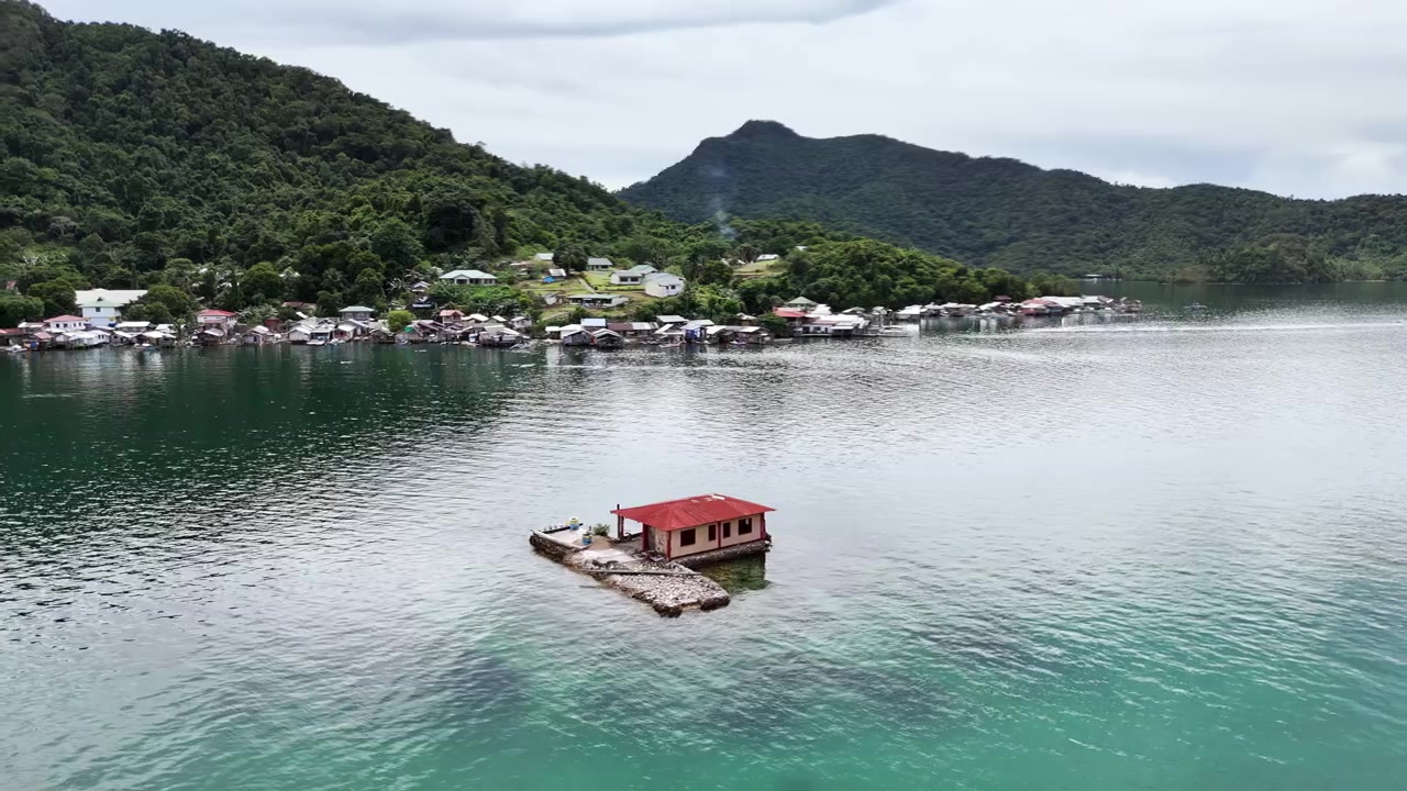 Orbit-optagelse af et ensomt hus på en sandbanke nær kysten, med kysthytter i baggrunden. Filmet i San Jose, Taytay, Palawan, Filippinerne. Dronen cirkler om motivet