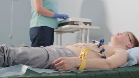 examen cardíaco en un hospital con un cardiógrafo profesional. el paciente se acuesta en una cama con sensores conectados.