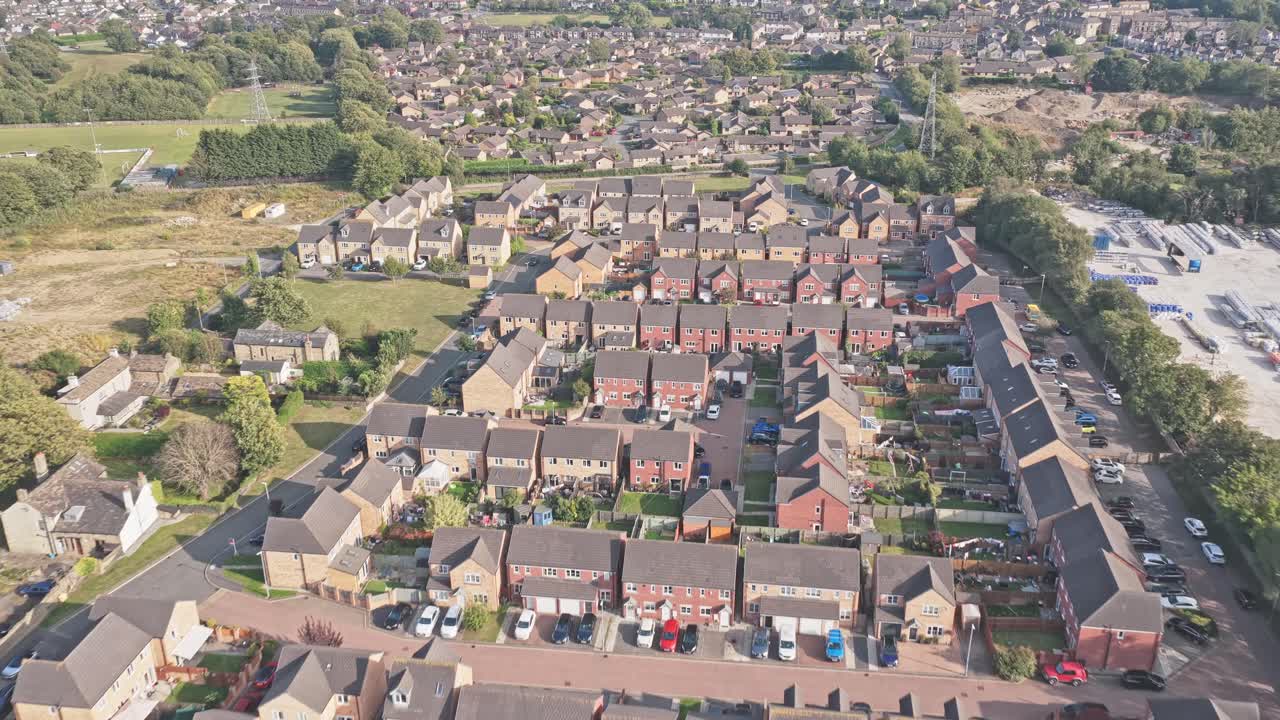 Ripresa aerea di un drone che sorvola velocemente Sunderland Way, Brighouse, Calderdale, West Yorkshire, Inghilterra, e rivela file ordinate di case nuove e meno recenti, prati verdi e la struttura stradale di una zona residenziale suburbana.
