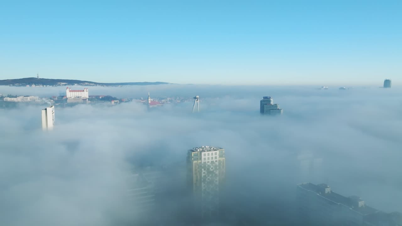 드론이 앞으로 이동하면서 태양빛의 공중 모험이 펼쳐지고, 밀집된 역전 구름을 통해 나타나는 브라티슬라바 성과 건물을 포착합니다.