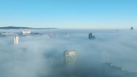 A-sunlit-aerial-adventure-unfolds-as-a-drone-moves-forward,-capturing-the-Bratislava-castle-and-buildings-emerging-through-dense-inversion-clouds