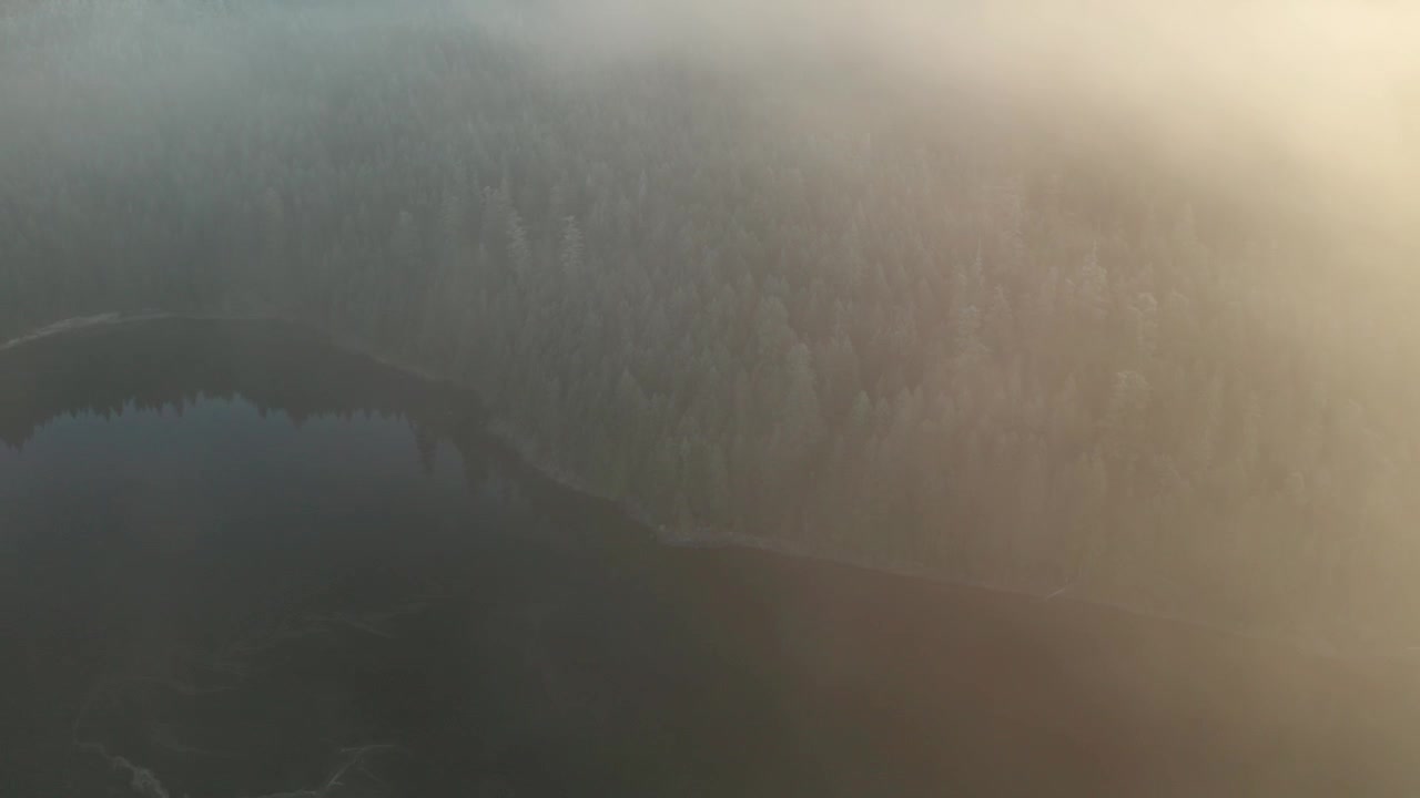 Luftfoto af tåget bjergsø ved solopgang, der bevæger sig baglæns gennem skyerne