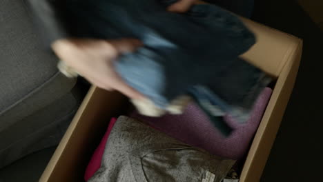 woman packing folded clothes into cardboard box preparing for new home move