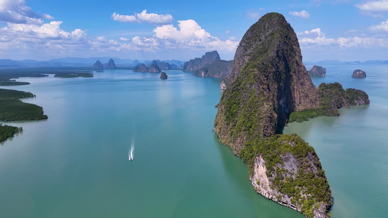 Drone footage captures stunning aerial views of Phang Nga Bay, showcasing limestone cliffs, turquoise waters, and a moving boat under clear skies