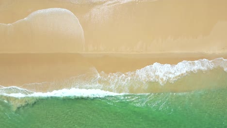 top down drone view over waves breaking at sandy beach