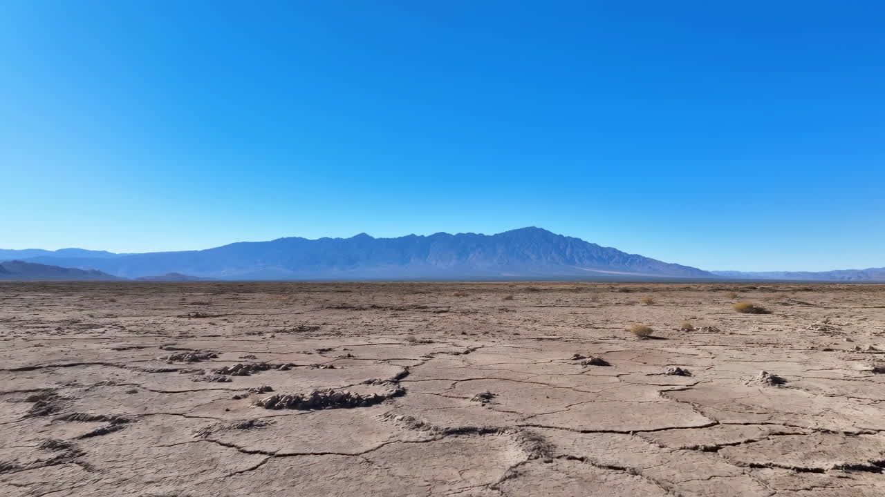 Terreno desertico crepato sotto un cielo blu intenso, ampia piana arida con crosta di sale poligonale e argilla inaridita, elementi in lontananza.