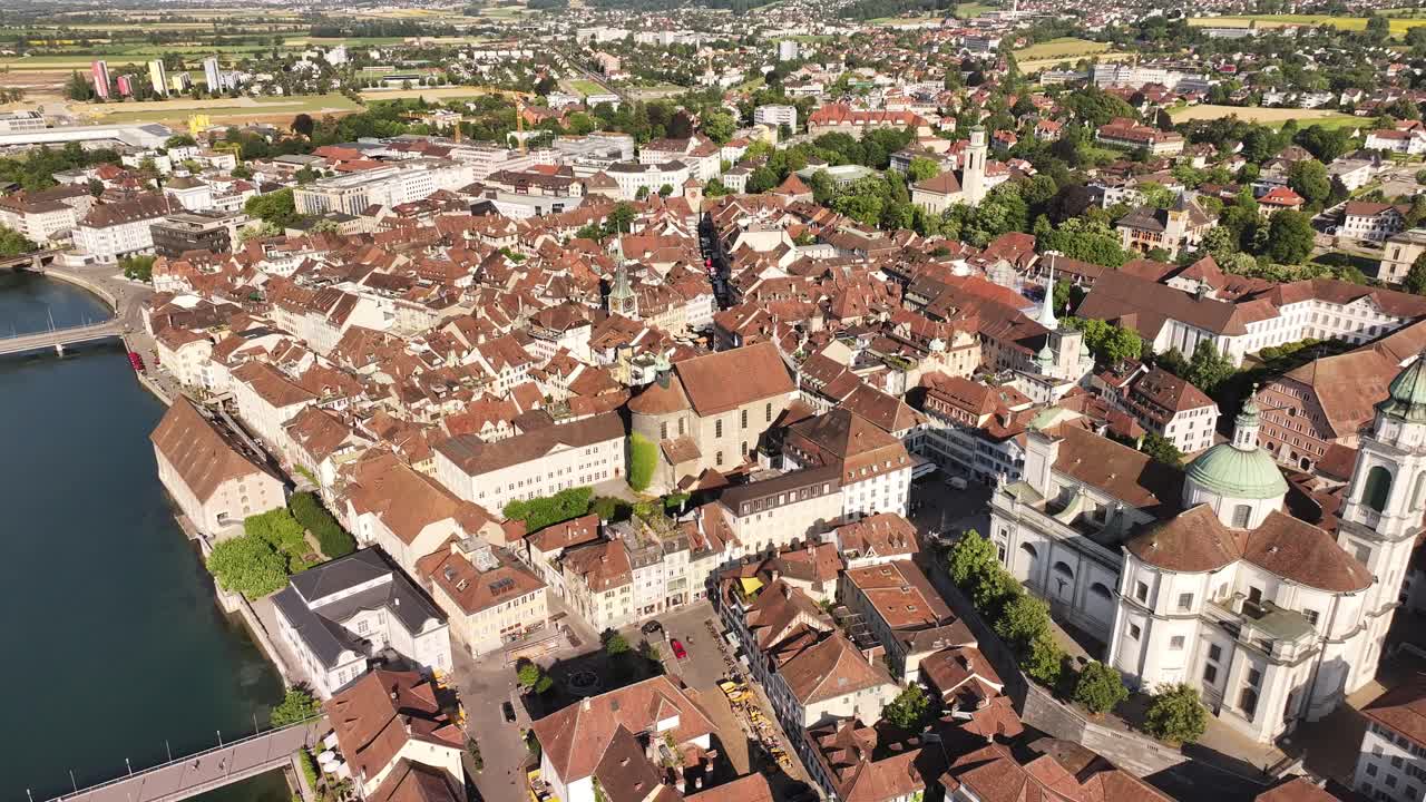 Aerial view showcases the city of Olten, Kanton Solothurn, Switzerland, with its historic rooftops and a prominent church at the center. The cityscape is nestled along a tranquil river