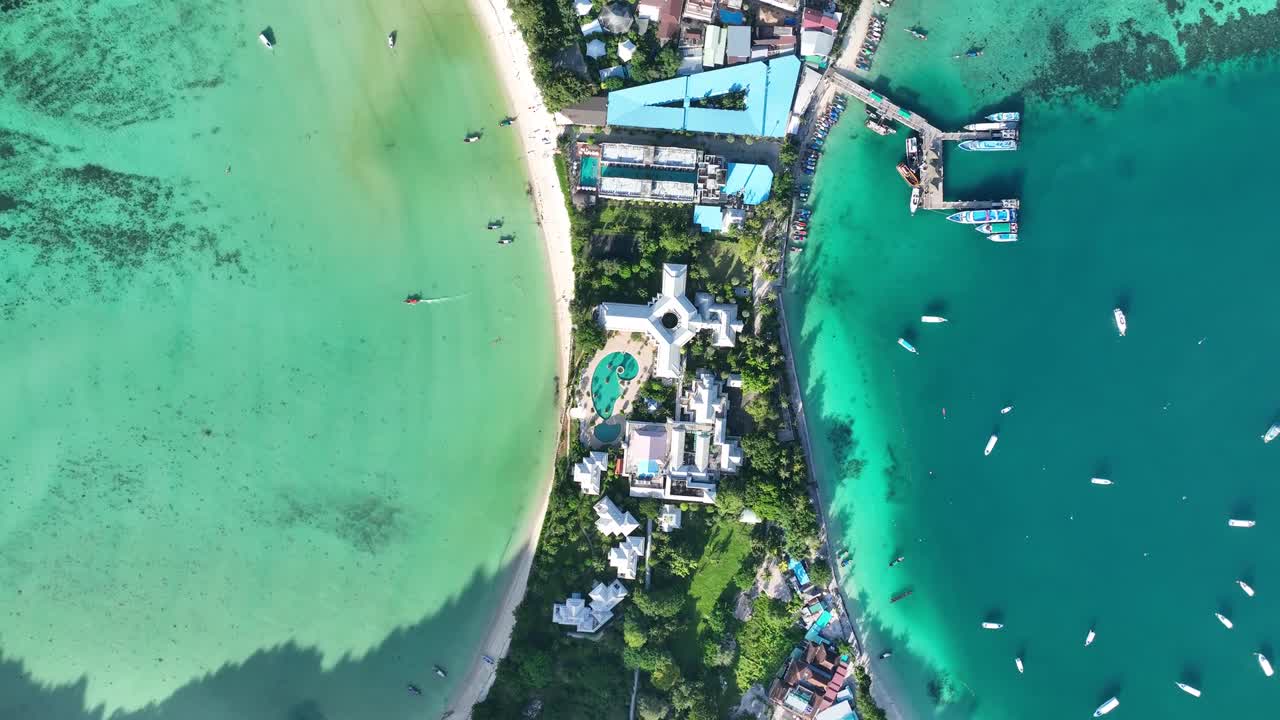 Luftfoto af Phuket, Thailand, der viser en lavvandet, grøn lagune, en dybblå marina, både, dokker og resort-bygninger, der ligger i den frodige, tropiske vegetation ved havet