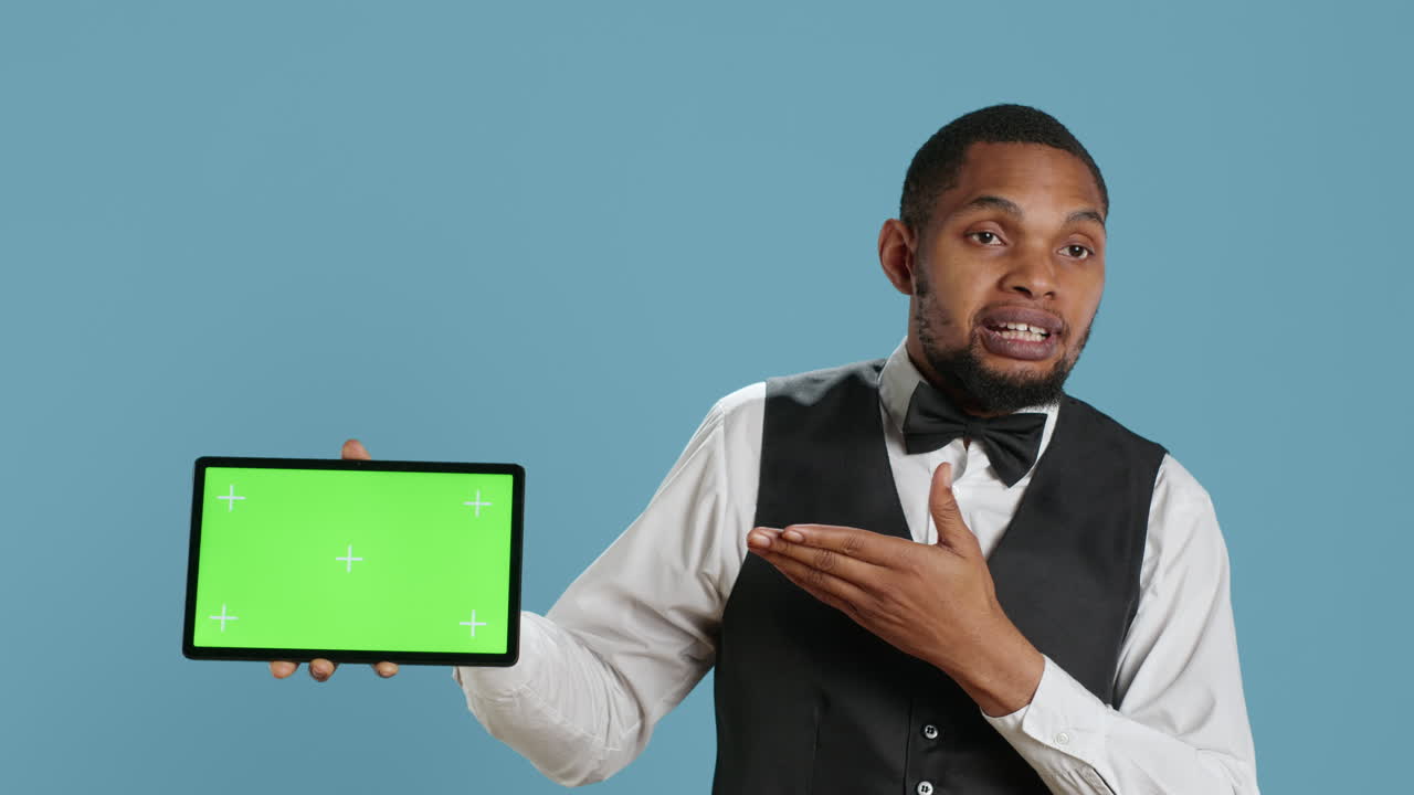 Doorkeeper bellboy poses with green screen on tablet at the hotel reception
