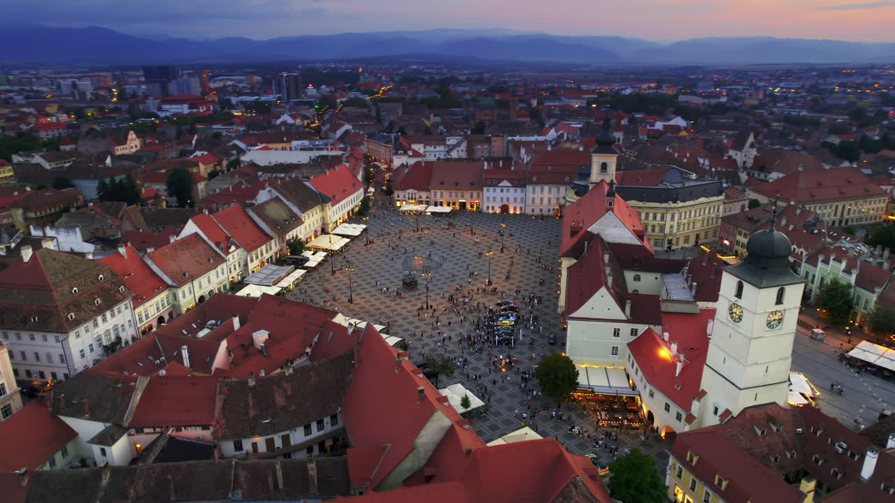 Lotniczy widok z drona na zabytkowe centrum Sybinu o zachodzie słońca, Rumunia. Wielki Rynek z katedrą ewangelicką w Sybinie i starymi budynkami wokół, wąskie uliczki, iluminacja