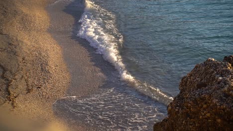 Slow-motion-waves-breaking-on-sandy-beach-with-rocks