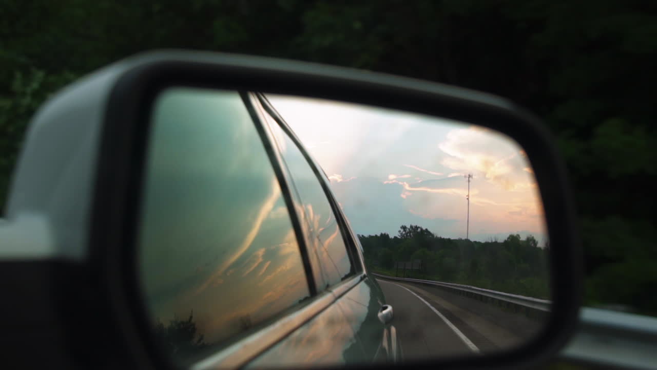 Cielo color zucchero filato all'ora d'oro nello specchietto laterale di un'auto in movimento al rallentatore