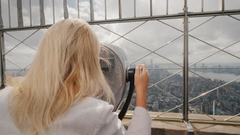 blonde woman looking through binoculars on the panorama of new york visit new york concept