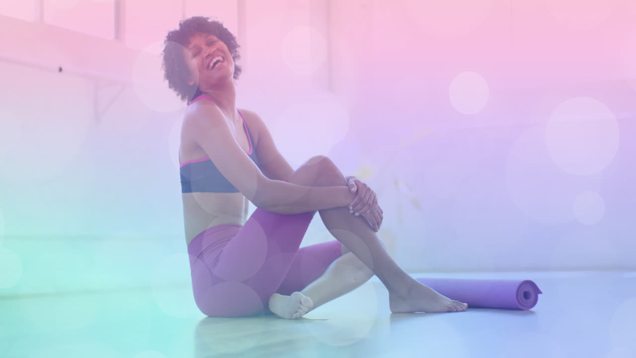 Sitting on floor with yoga mat, woman smiling over pastel bokeh animation
