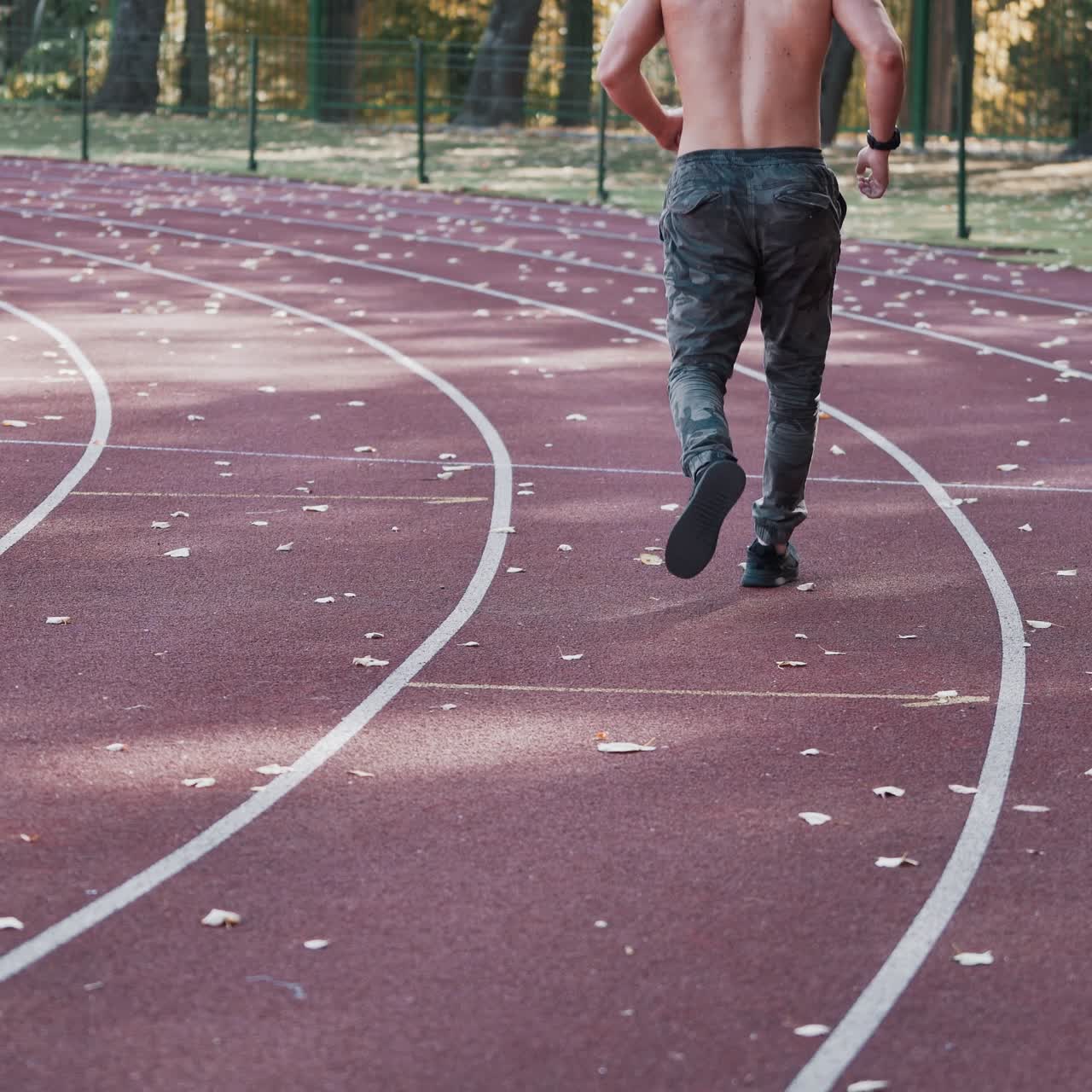 Back view of a man jogging on the stadium. Young athlete practices running outside on athletics track in autumn.