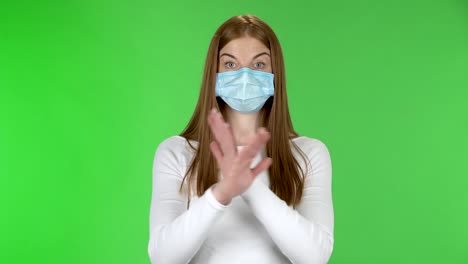 retrato de una joven con una máscara de protección médica mirando a la cámara y gesticulando estrictamente con las manos cruzadas haciendo forma de x que significa negación diciendo no