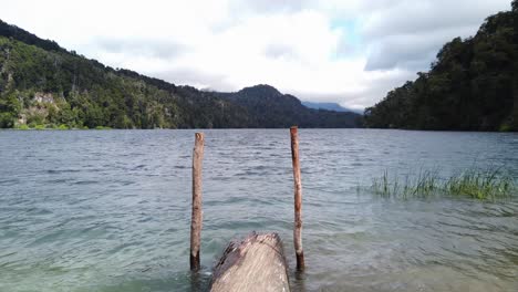 POV-view-walking-on-driftwood-log-on-calm-mountain-lake,-overcast