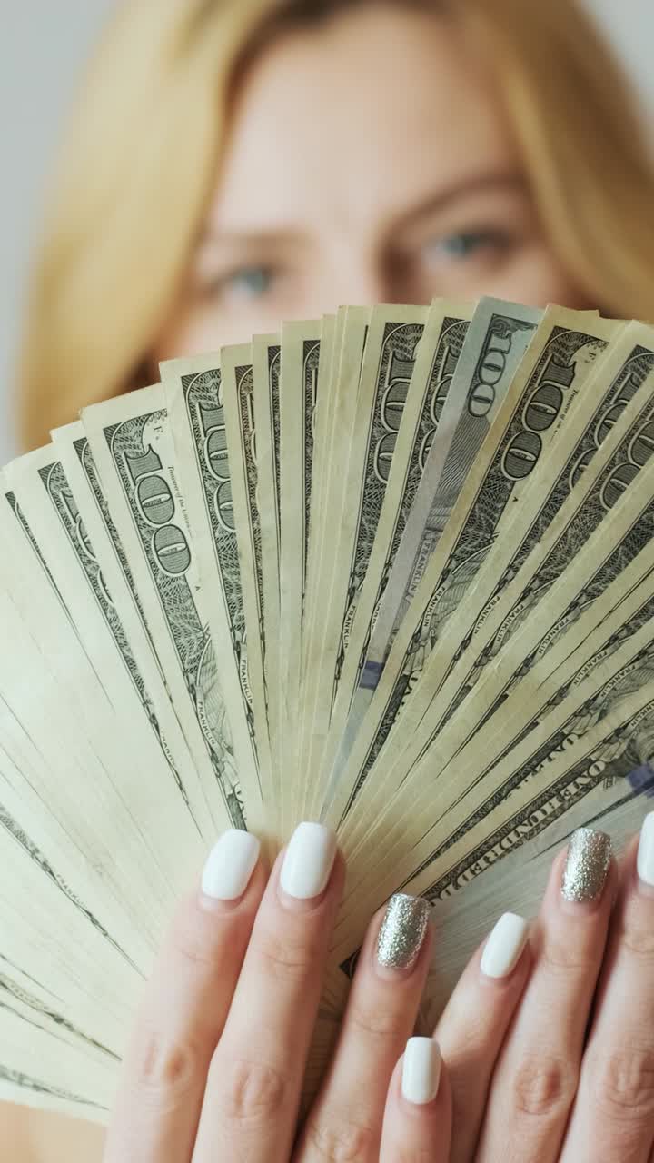 Donna che tiene una mazzetta a ventaglio di banconote da cento dollari