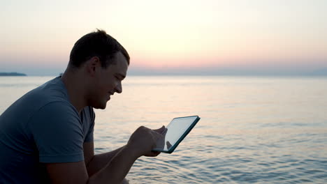 Young-man-by-the-sea-typing-message-on-pad