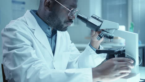black doctor performing medical test with microscope and taking notes in lab