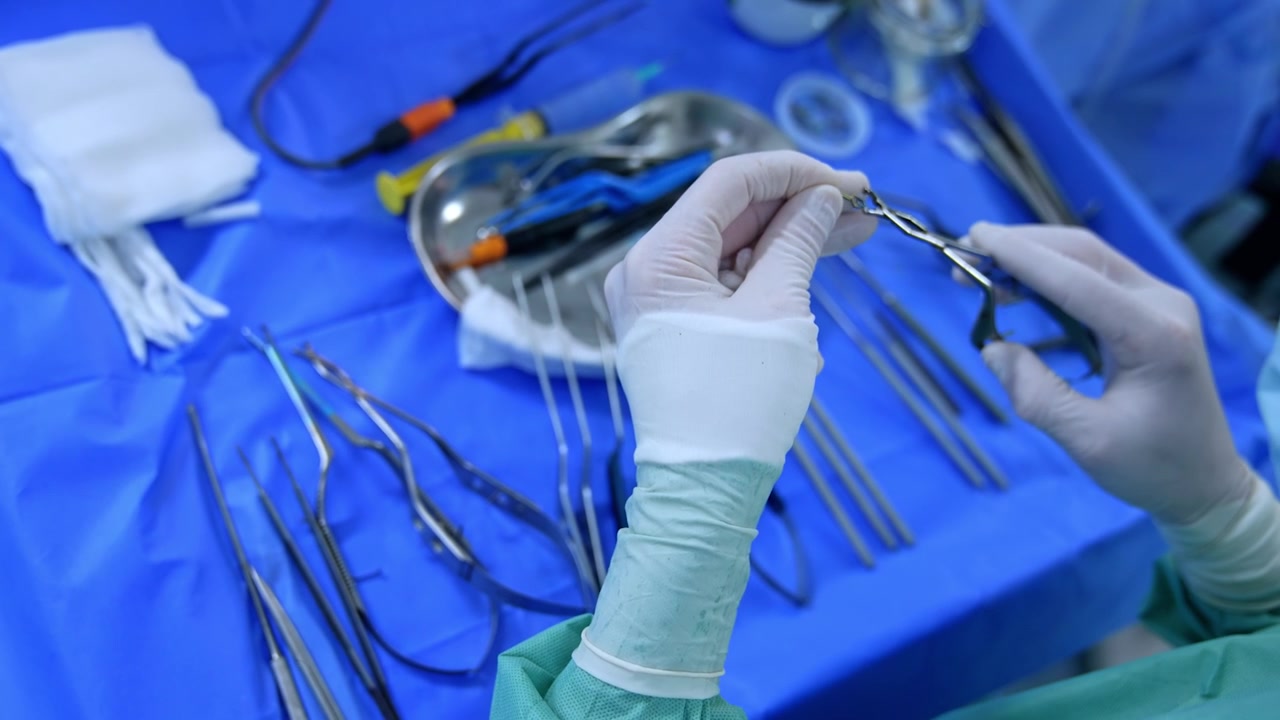 Hands in latex gloves take the tools from the surgical stand. Medic prepares tools for the surgery. Close up.