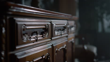 closeup carved chest of drawers in dark interior. antique wood dresser indoors.