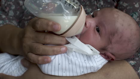 close up shot of a newborn infant baby cradled in his mother’s arms feeding on a bottle of breast milk