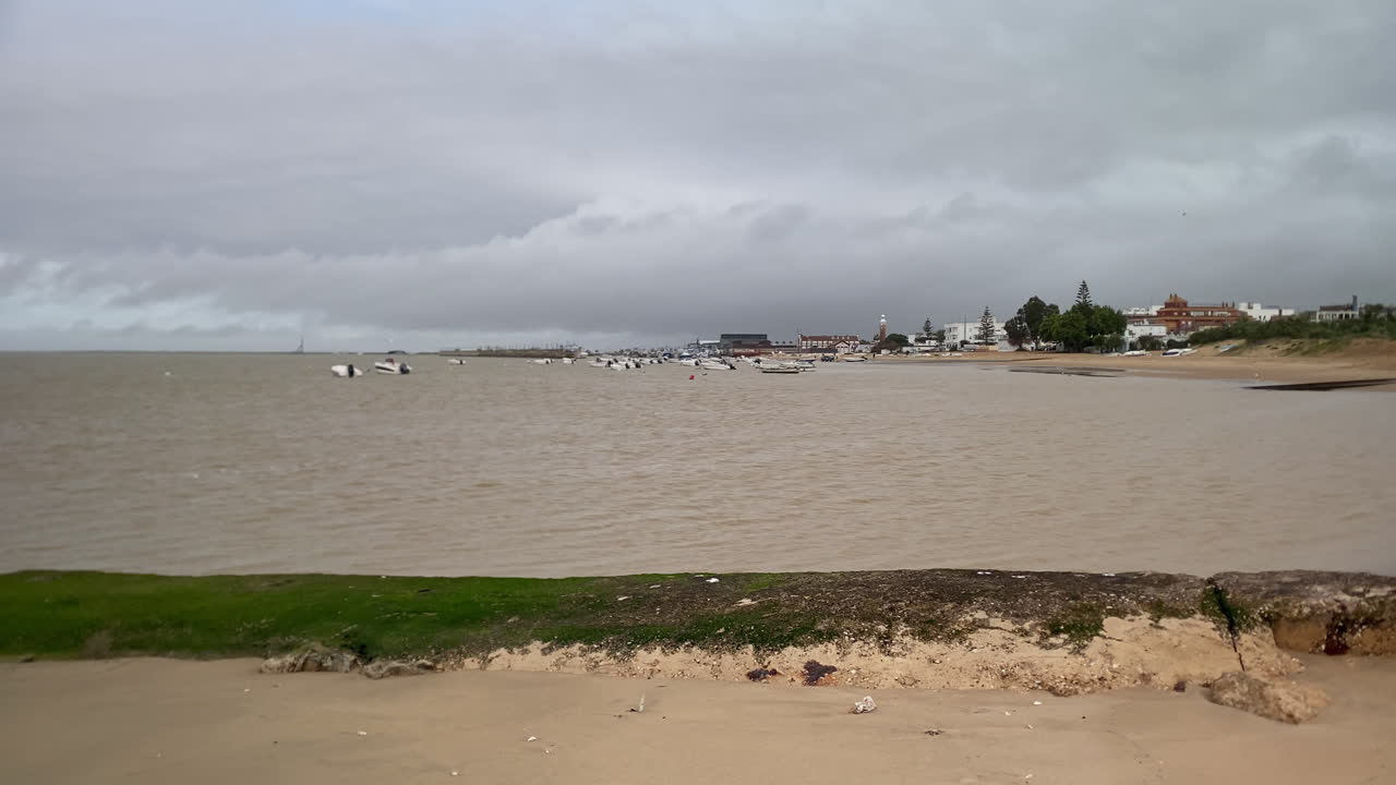 Sanlúcar de Barrameda, Spagna, che mostra il porto costiero con molte piccole barche ormeggiate su acqua torbida sotto un cielo nuvoloso.
