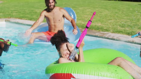 Grupo-Diverso-De-Amigos-Divirtiéndose-Jugando-Con-Pistolas-De-Agua-En-Inflables-En-La-Piscina