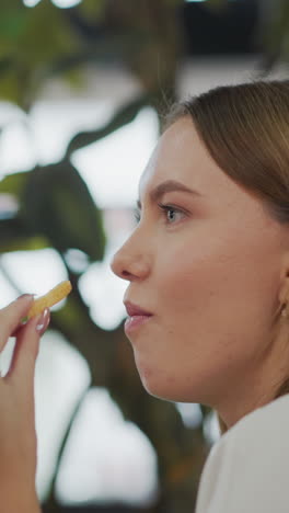 fotografía en primer plano de una mujer con uñas pulidas comiendo papas fritas crujientes en un entorno de comedor casual, con un fondo suave y borroso con iluminación cálida y personas entrando en el centro comercial