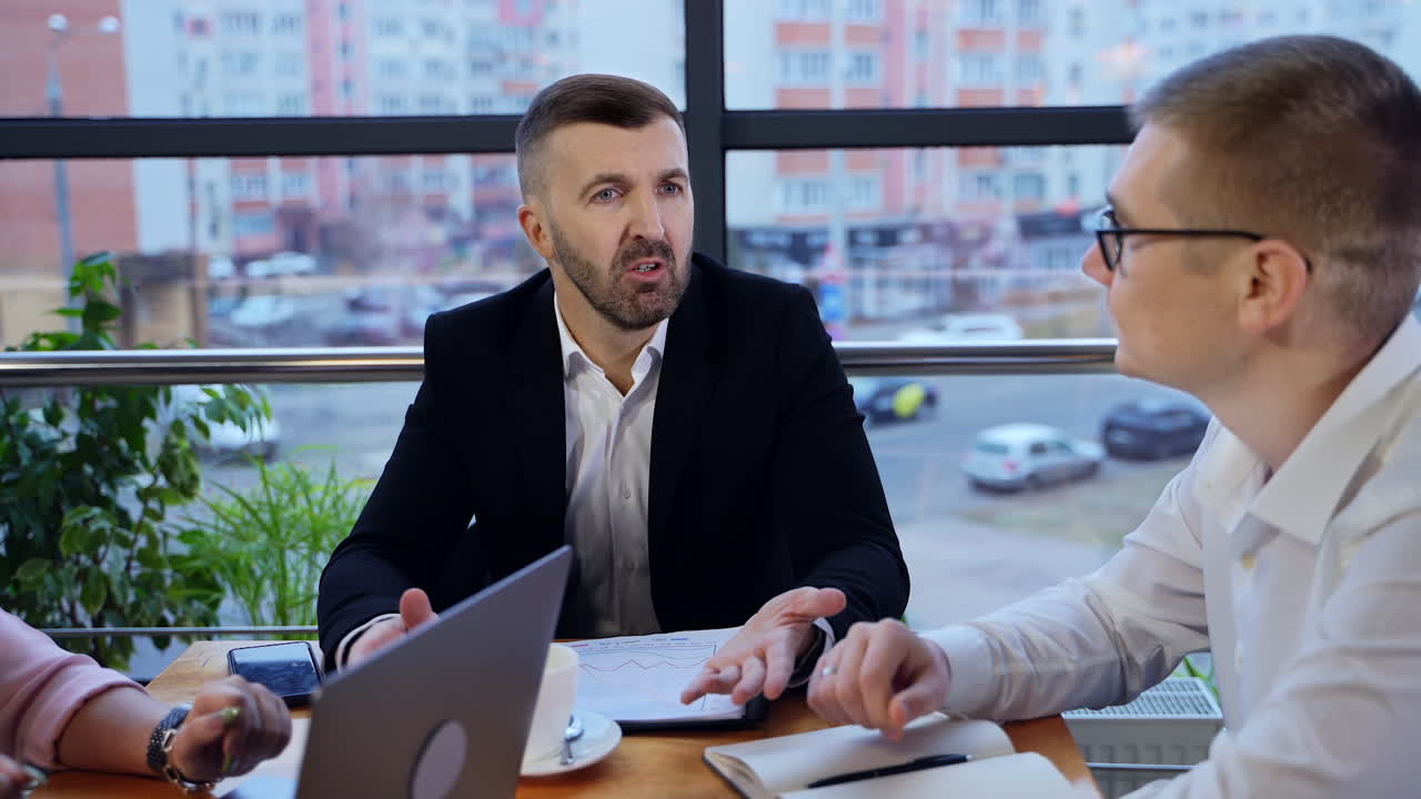 Manager aziendale che parla con il suo dipendente in ufficio. Team di lavoro che discute questioni lavorative seduto al tavolo. Paesaggio urbano sullo sfondo