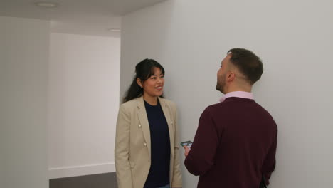 male teacher using mobile phone passing female colleague as they walk along corridor in school building