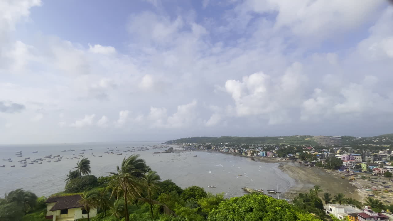 A stunning 4K aerial drone view of Uttan Beach in Mumbai, Maharashtra, featuring its sandy shores, lush green trees, and the cityscape in the background under a cloudy sky