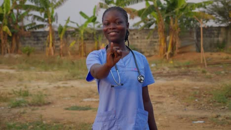 black african female doctor nurse in blue lab cost with stethoscope saying ove with hand gesture language smiling in front of camera