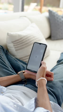 vertical video: relaxing on couch, person using smartphone at home, enjoying leisure time