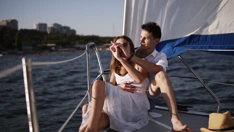 romantic young couple enjoying time together on small cruise ship sailing on open sea. woman and man in love on boat travel sailing during vacation, guy holding a hand of his girlfriend while sitting together on a bow deck