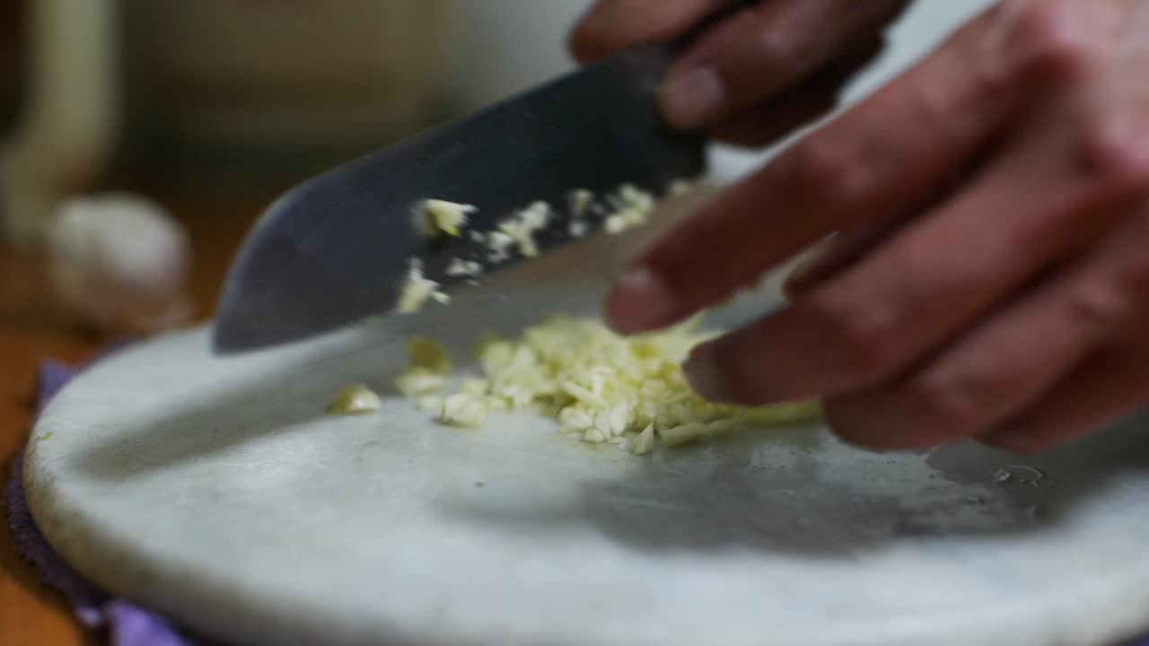 Aglio tritato su tagliere di marmo bianco usando un coltello da cucina, filmato in primo piano al rallentatore