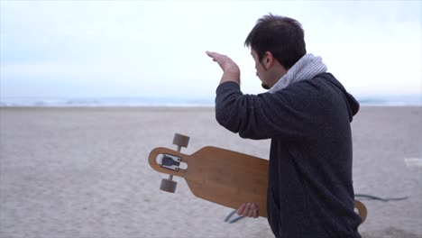 Surfer-Am-Strand,-Der-Mit-Der-Langen-Hand-Auf-Das-Meer-Zeigt-Und-über-Seinen-Zustand-Spricht