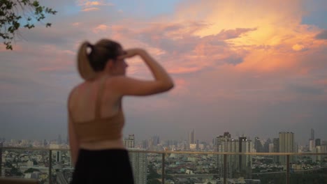 Woman-on-rooftop-searching-for-something-in-the-city-with-buildings-on-a-sunset,-static-closeup