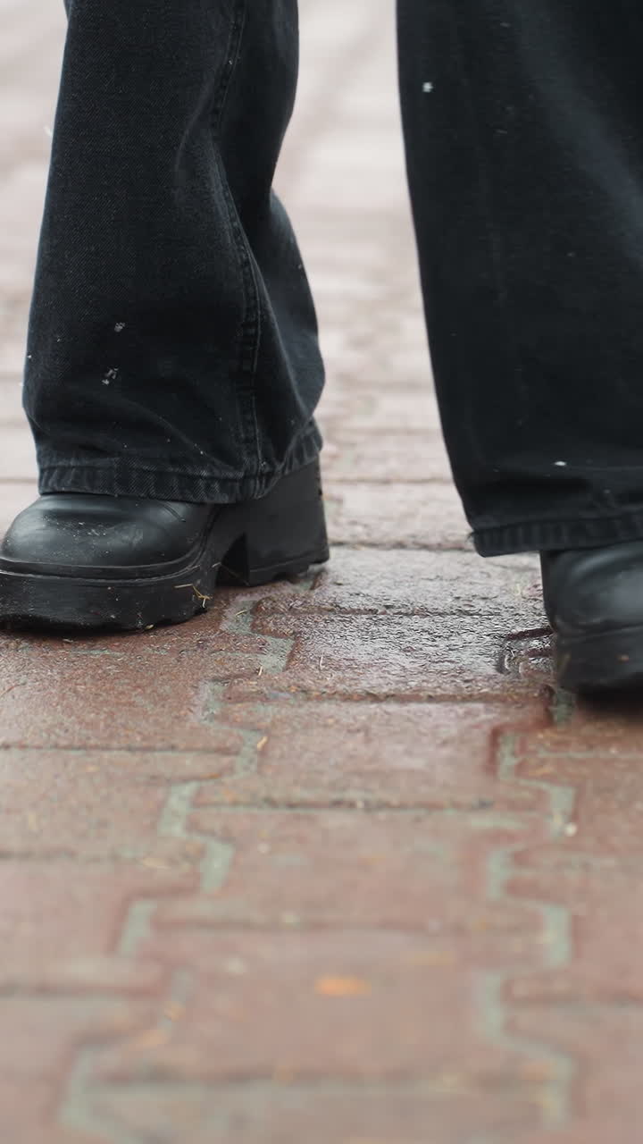 Foot of person wearing black trousers and black boots turning on wet ground, creating ripples on surface, showcasing motion in urban or outdoor setting, walking on rainy day or after rain