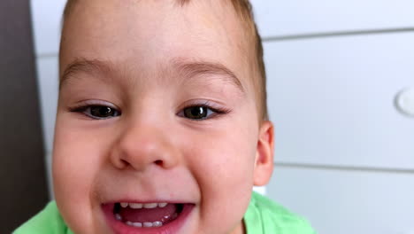 happy smiling toddler boy looking at camera. playful kid wants to touch camera and then drinks from a straw. close up.