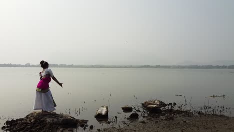 Una-Bailarina-De-Bharatnatyam-Que-Muestra-Una-Pose-Clásica-De-Bharatnatyam-En-La-Naturaleza-Del-Lago-Vadatalav,-Pavagadh