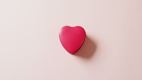 Overhead-video-of-red-heart-shaped-gift-box,-on-pale-pink-background-with-copy-space