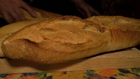 agarra con la mano panes de pan galego largo y fresco para apilarlos en la tabla de cortar de madera