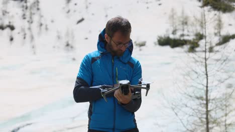 hombre en chaqueta azul de invierno se encuentra al aire libre en la nieve y lanza un dron de la mano
