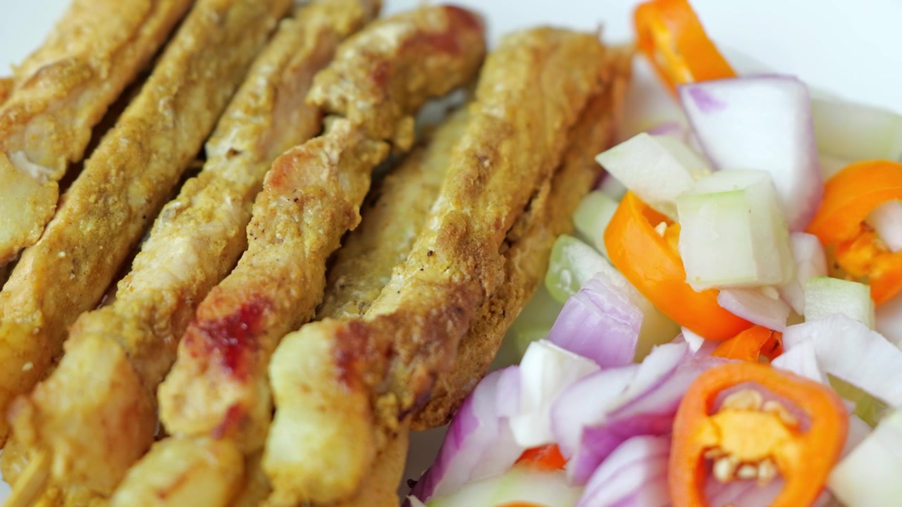 Primo piano di molti spiedini satay di maiale grigliati disposti insieme, con bordi dorati e carbonizzati, carne tenera e una ricca salsa di arachidi per intingere